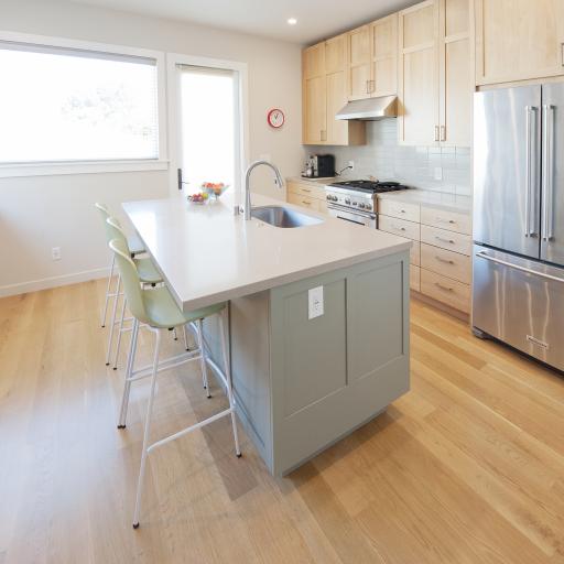 The center of this kitchen has a large island that has an eating bar and a built in sink. Light wood cabinets along the right side match the hardwood floors and set off the stunning stainless steel appliances.