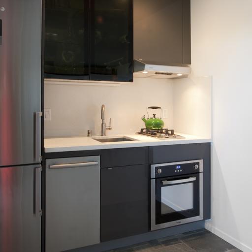 The kitchen area has a stainless steel refrigerator, 2-burner stove, micro-oven and sink with cabinets creates a compact, functional space. This photo is from El Cerrito Micro Apartment designed by Susan L. Wootan