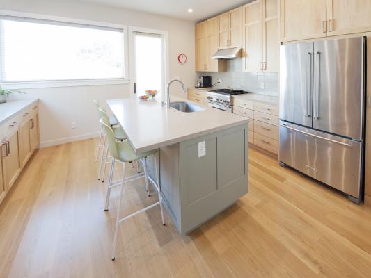 The center of this kitchen has a large island that has an eating bar and a built in sink. Light wood cabinets along the right side match the hardwood floors and set off the stunning stainless steel appliances.