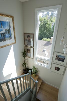 Another angle looking down the bright stairway which features the same gray trim and light wood floors creating a cohesive space. A large window and framed artwork on the walls completes the landing.