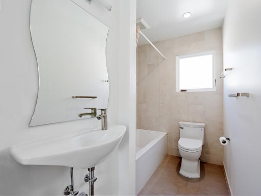 The full bath is compact and clean with a hanging sink, low-flow toilet, and neutral colors. The sink is on the left with the bathroom in the back corner. A window and the toilet are on the far wall.