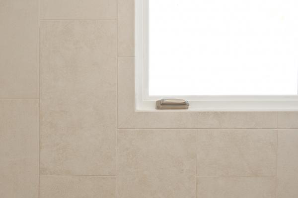 A close up of the tile wall and corner of the window. The tiles are light neutral colored and slightly mottled.