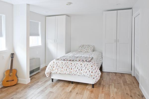 A white room with a Murphy bed in the down position flanked by two tall cupboards. Two windows are on the left side of the room and there's a guitar in a corner.